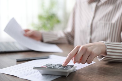 Photo of Budget. Woman with paperwork and calculator at wooden desk indoors, closeup