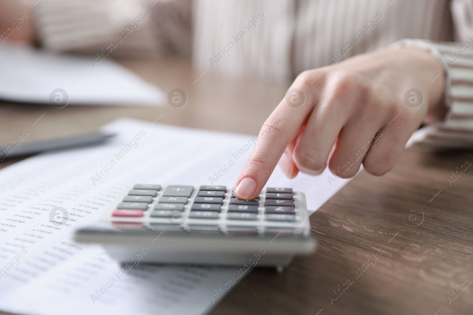 Photo of Budget. Woman with paperwork and calculator at wooden desk indoors, closeup