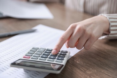 Photo of Budget. Woman with paperwork and calculator at wooden desk indoors, closeup