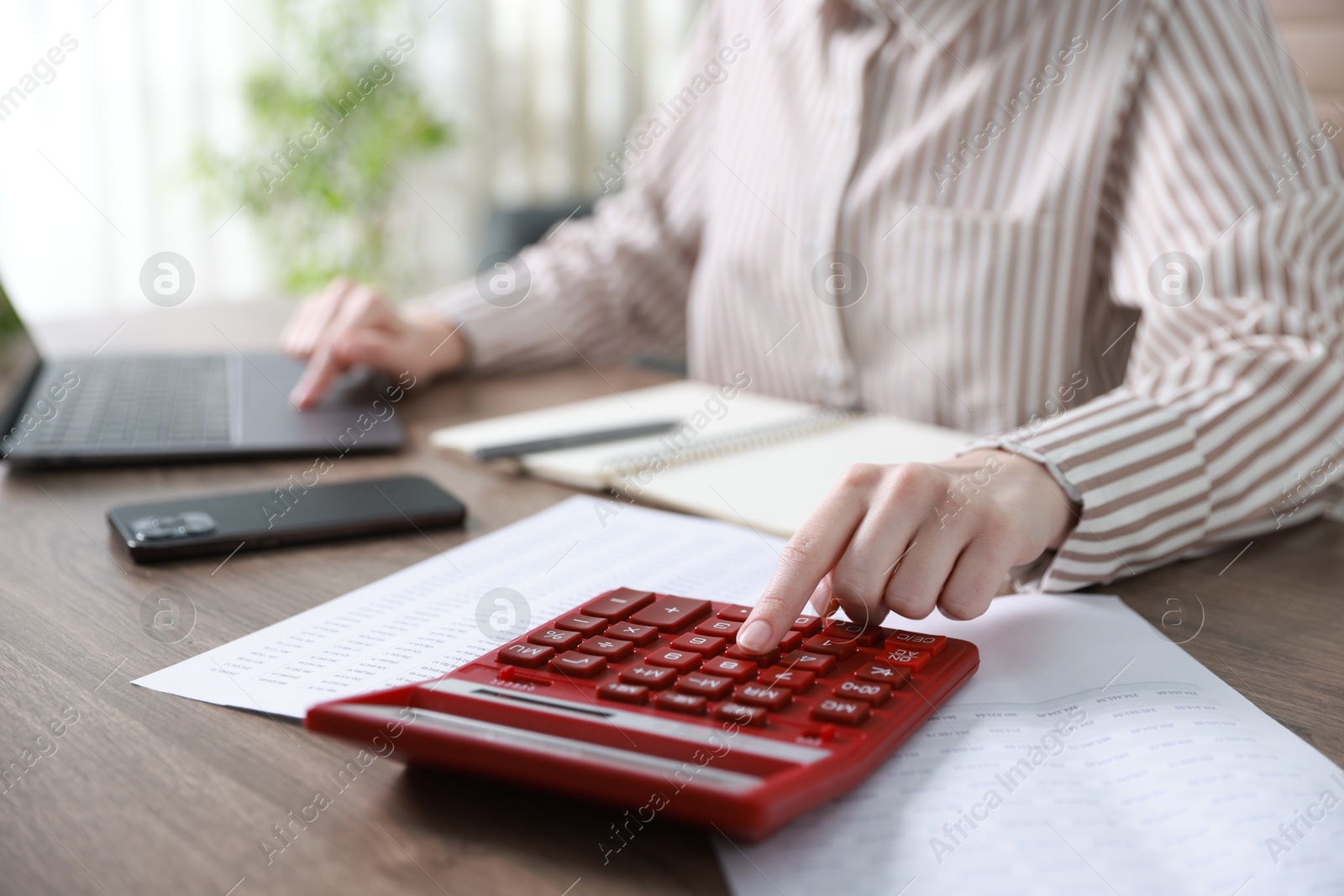 Photo of Budget. Woman with calculator, paperwork and laptop at wooden desk indoors, closeup