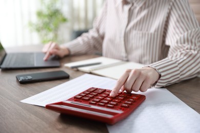 Photo of Budget. Woman with calculator, paperwork and laptop at wooden desk indoors, closeup