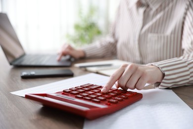 Photo of Budget. Woman with calculator, paperwork and laptop at wooden desk indoors, closeup