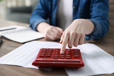 Photo of Budget. Woman with paperwork and calculator at wooden desk indoors, closeup