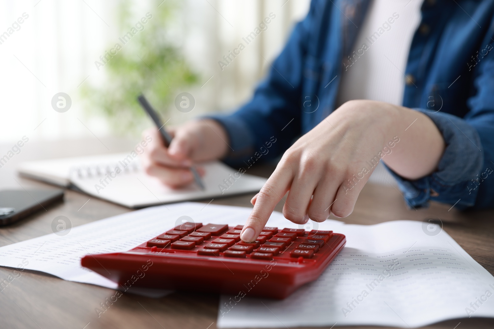 Photo of Budget. Woman with paperwork and calculator at wooden desk indoors, closeup