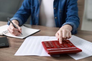 Photo of Budget. Woman with paperwork and calculator at wooden desk indoors, closeup