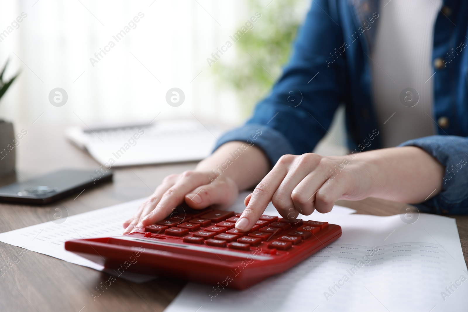 Photo of Budget. Woman with paperwork and calculator at wooden desk indoors, closeup