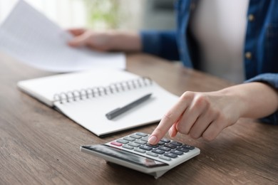 Photo of Budget. Woman with paperwork and calculator at wooden desk indoors, closeup