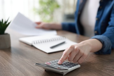 Photo of Budget. Woman with paperwork and calculator at wooden desk indoors, closeup