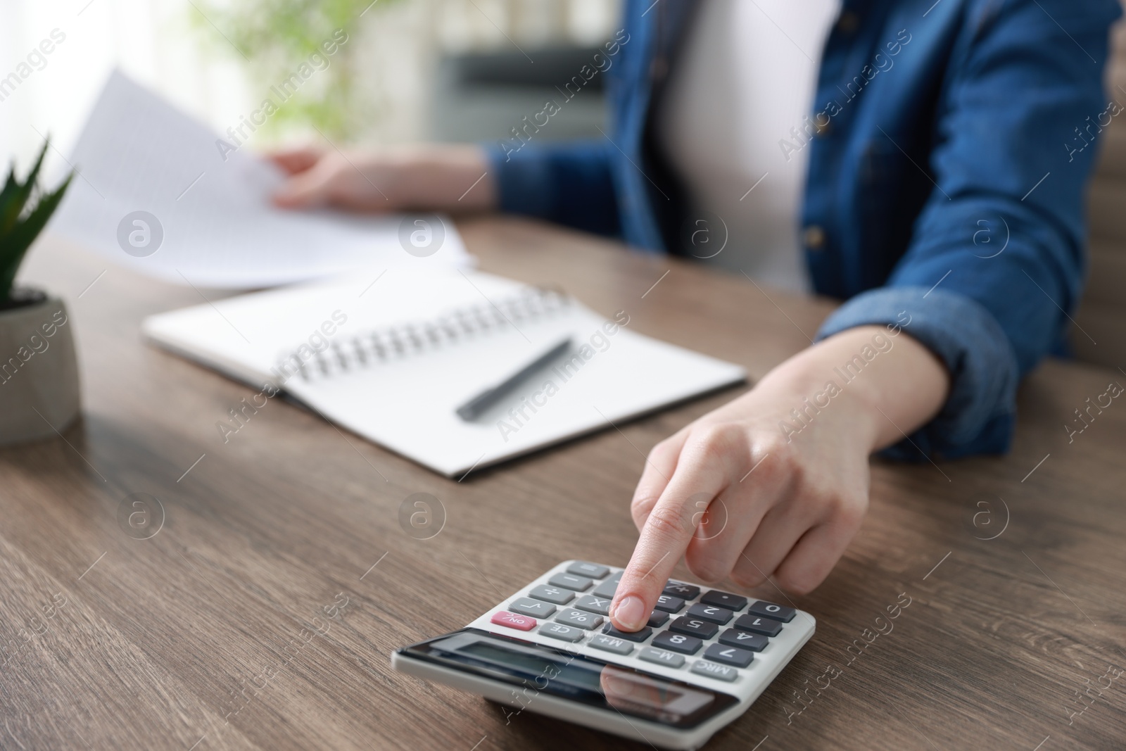 Photo of Budget. Woman with paperwork and calculator at wooden desk indoors, closeup