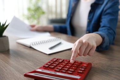 Photo of Budget. Woman with paperwork and calculator at wooden desk indoors, closeup