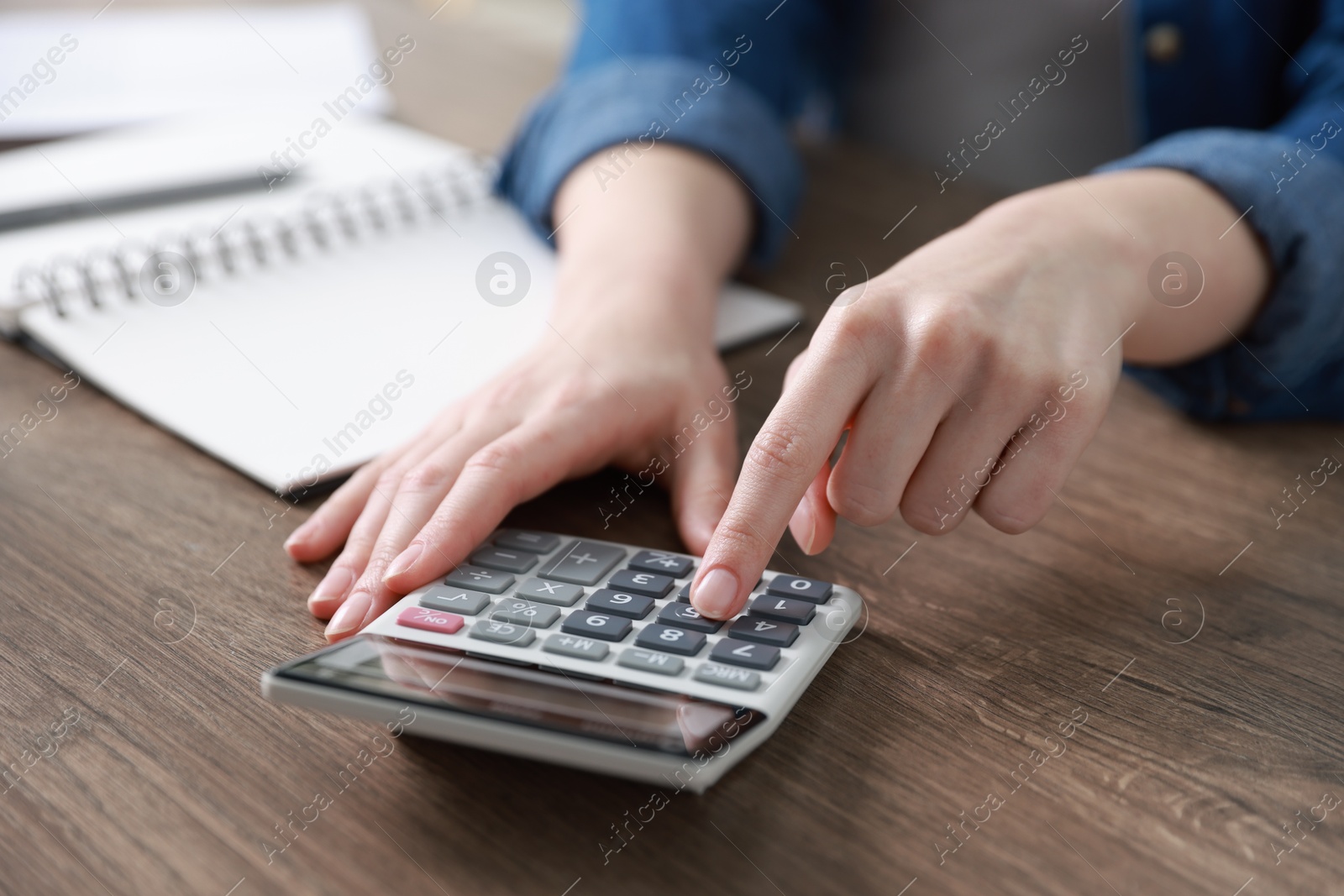 Photo of Budget. Woman with paperwork and calculator at wooden desk indoors, closeup