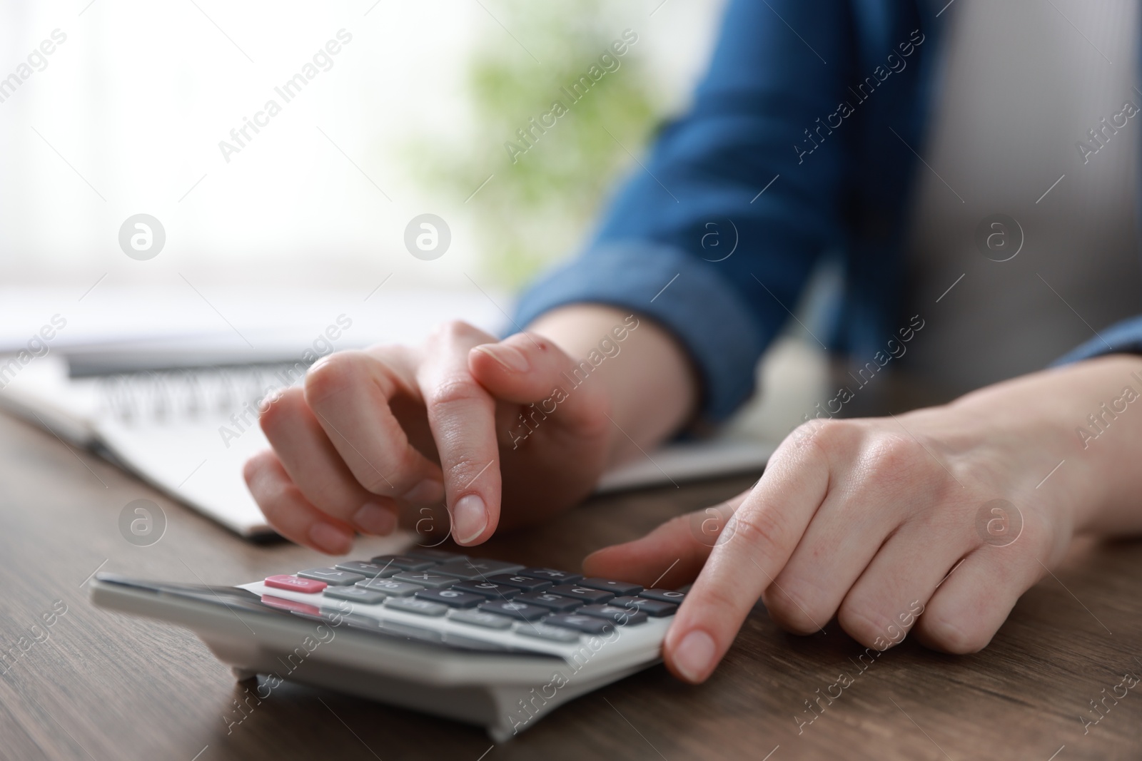 Photo of Budget. Woman with paperwork and calculator at wooden desk indoors, closeup