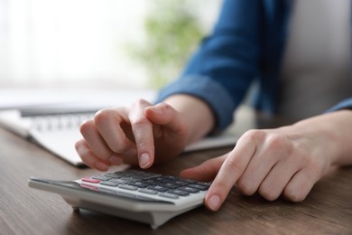 Photo of Budget. Woman with paperwork and calculator at wooden desk indoors, closeup