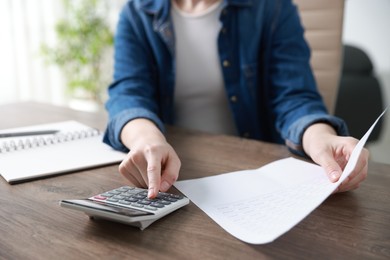 Photo of Budget. Woman with paperwork and calculator at wooden desk indoors, closeup