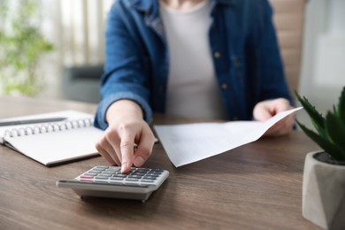 Photo of Budget. Woman with paperwork and calculator at wooden desk indoors, closeup