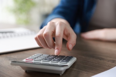 Photo of Budget. Woman with paperwork and calculator at wooden desk indoors, closeup