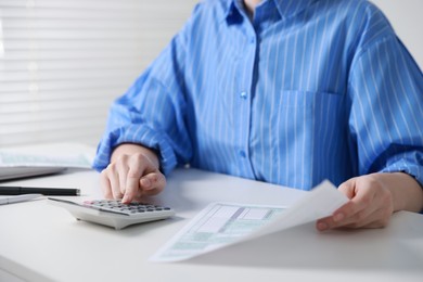 Photo of Budget. Woman with paperwork and calculator at white desk indoors, closeup