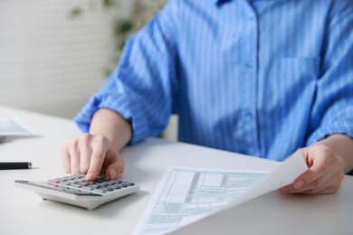 Photo of Budget. Woman with paperwork and calculator at white desk indoors, closeup