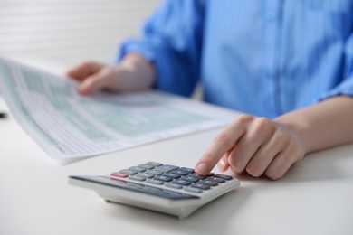 Photo of Budget. Woman with paperwork and calculator at white desk indoors, closeup