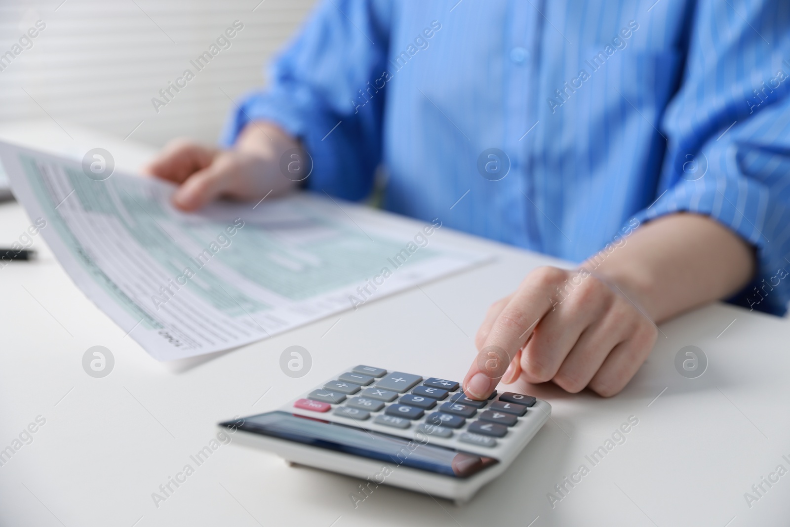 Photo of Budget. Woman with paperwork and calculator at white desk indoors, closeup