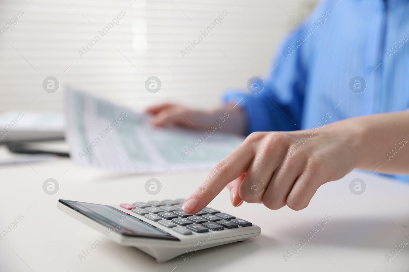 Photo of Budget. Woman with paperwork and calculator at white desk indoors, closeup