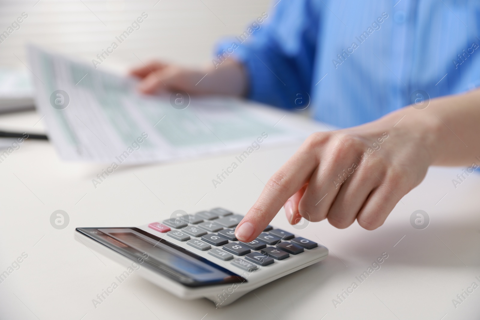 Photo of Budget. Woman with paperwork and calculator at white desk indoors, closeup