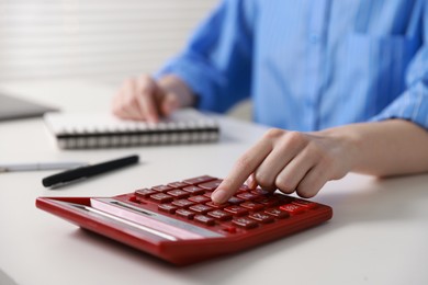 Photo of Budget. Woman with paperwork and calculator at white desk indoors, closeup