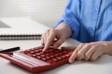 Photo of Budget. Woman with paperwork and calculator at white desk indoors, closeup