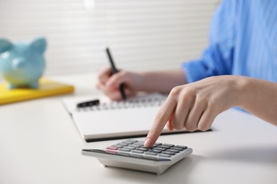 Photo of Budget. Woman with paperwork and calculator at white desk indoors, closeup