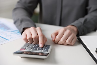 Photo of Budget. Woman with paperwork and calculator at white desk indoors, closeup