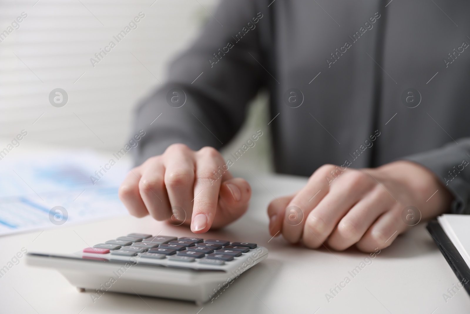 Photo of Budget. Woman with paperwork and calculator at white desk indoors, closeup