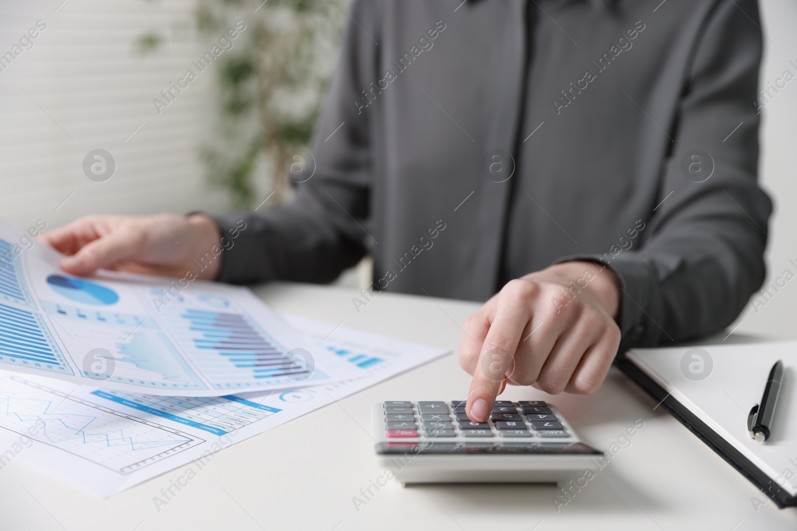 Photo of Budget. Woman with paperwork and calculator at white desk indoors, closeup