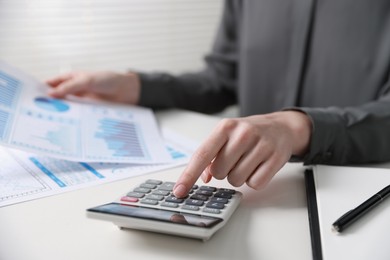 Photo of Budget. Woman with paperwork and calculator at white desk indoors, closeup