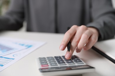 Photo of Budget. Woman with paperwork and calculator at white desk indoors, closeup