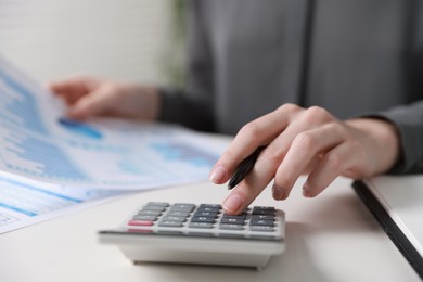 Photo of Budget. Woman with paperwork and calculator at white desk indoors, closeup