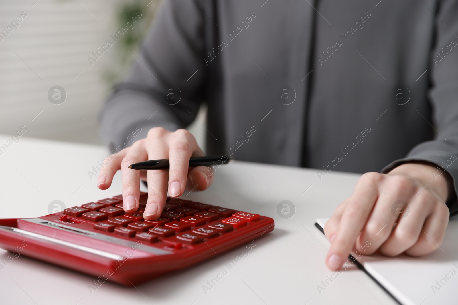 Photo of Budget. Woman with paperwork and calculator at white desk indoors, closeup