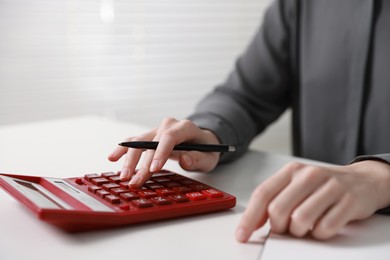 Photo of Budget. Woman with paperwork and calculator at white desk indoors, closeup