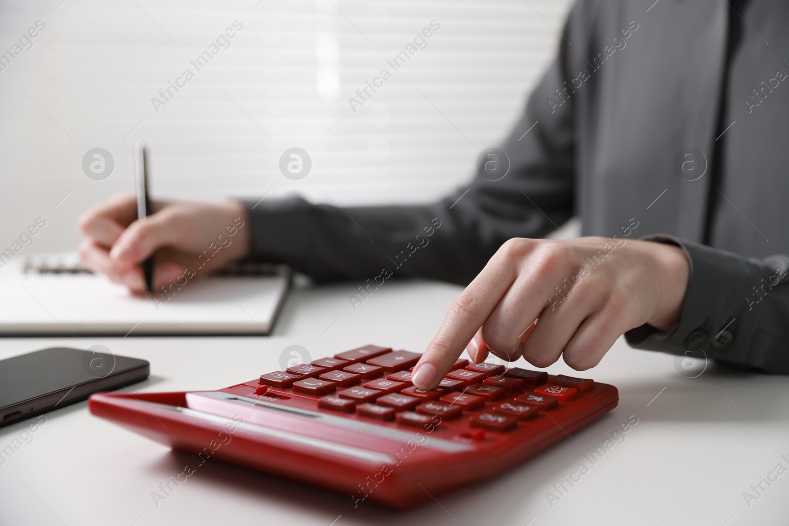 Photo of Budget. Woman with paperwork and calculator at white desk indoors, closeup