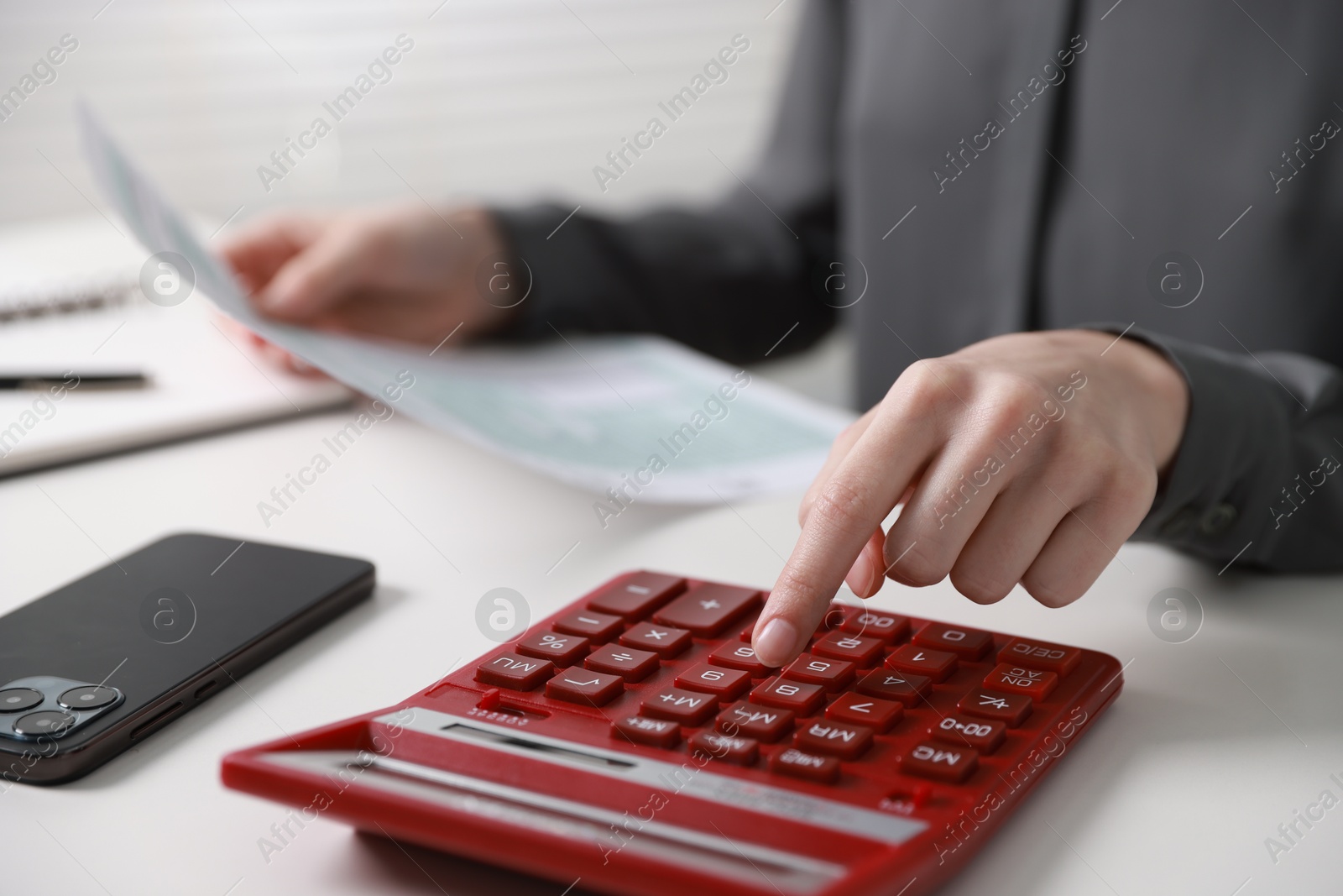 Photo of Budget. Woman with paperwork and calculator at white desk indoors, closeup