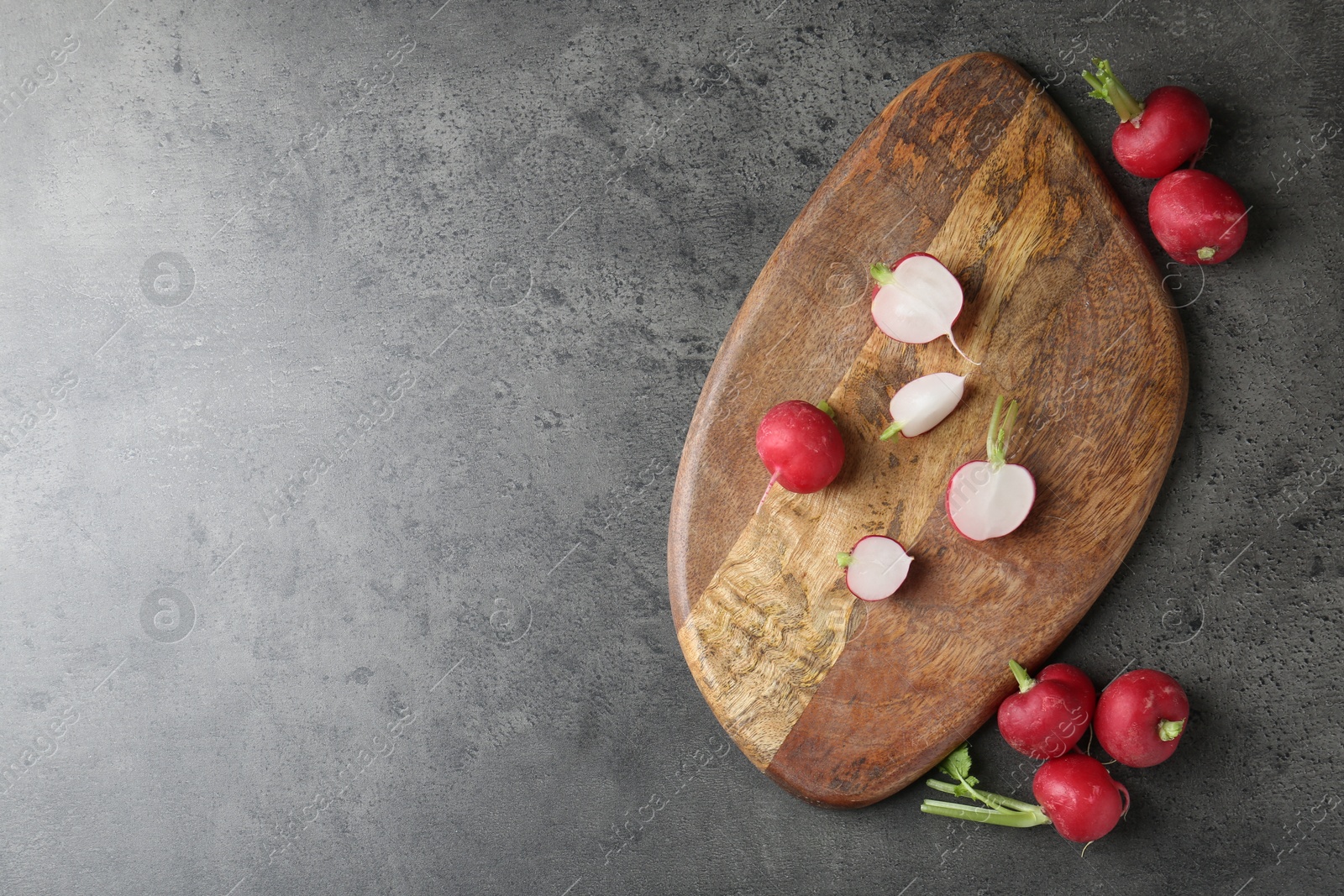 Photo of Cutting board with radishes on grey table, flat lay. Space for text