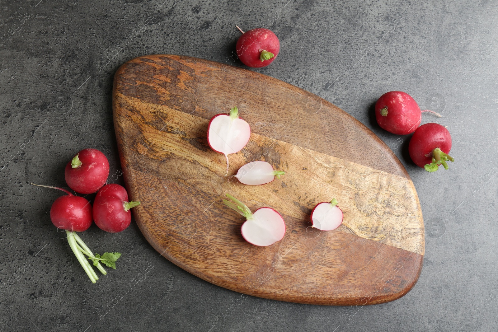 Photo of Cutting board with radishes on grey table, flat lay