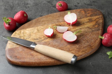 Photo of Cutting board with radishes and knife on grey table, closeup