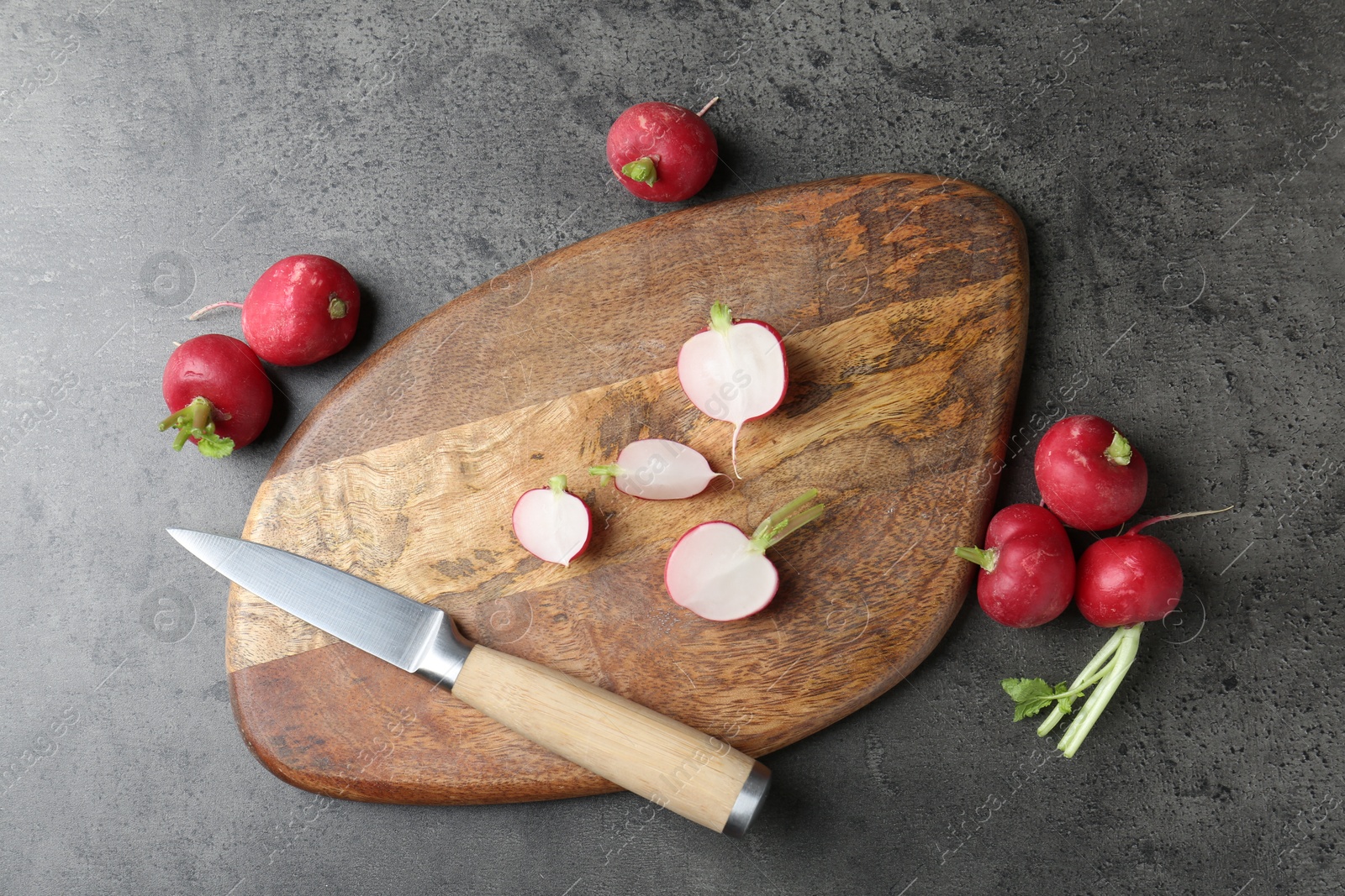 Photo of Cutting board with radishes and knife on grey table, flat lay