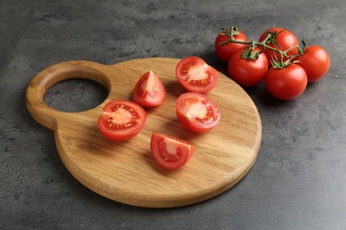 Photo of Cutting board with tomatoes on grey table, closeup