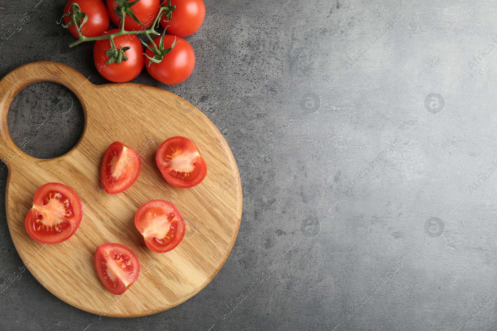 Photo of Cutting board with tomatoes on grey table, top view. Space for text