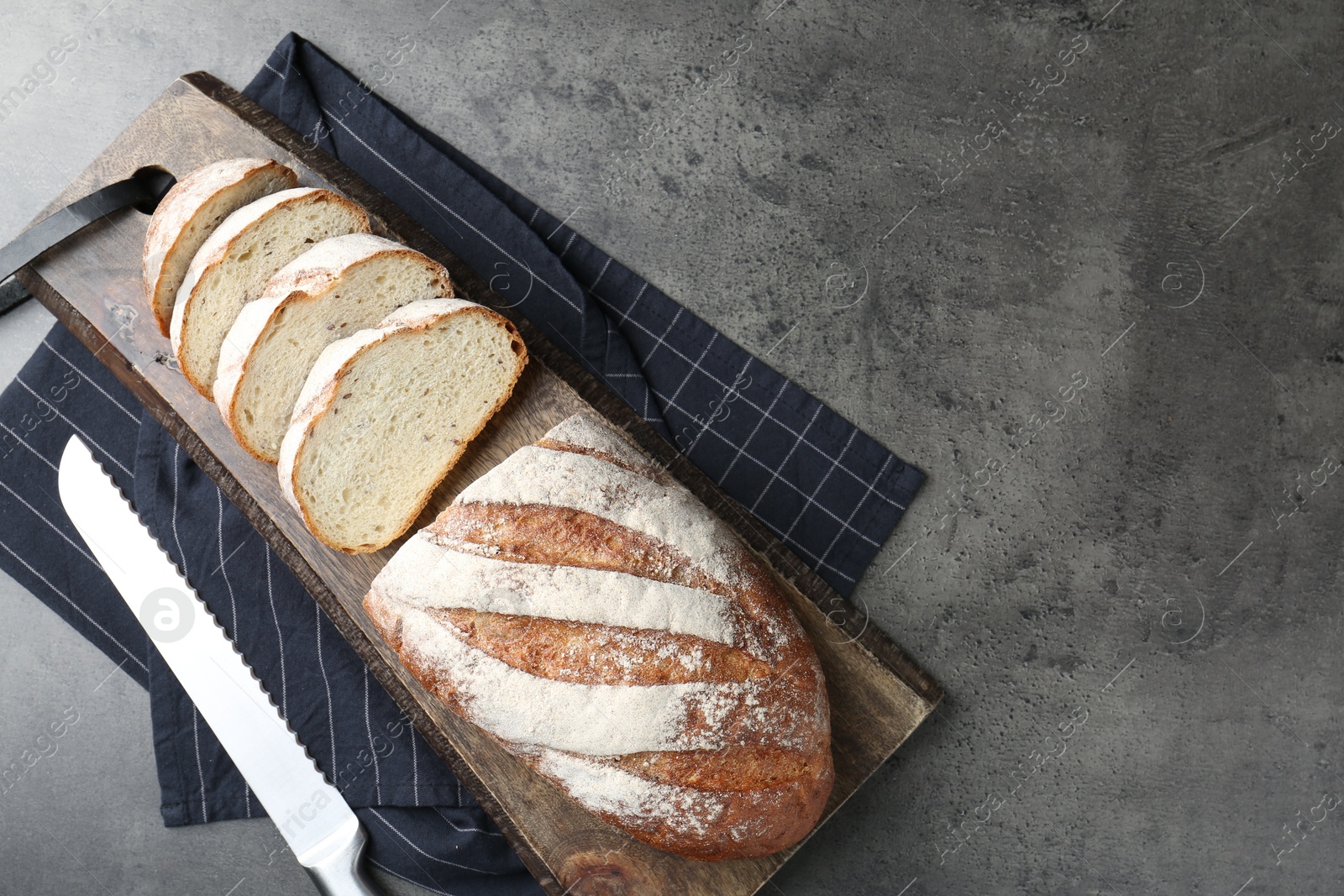 Photo of Cutting board with fresh bread and knife on grey table, top view. Space for text