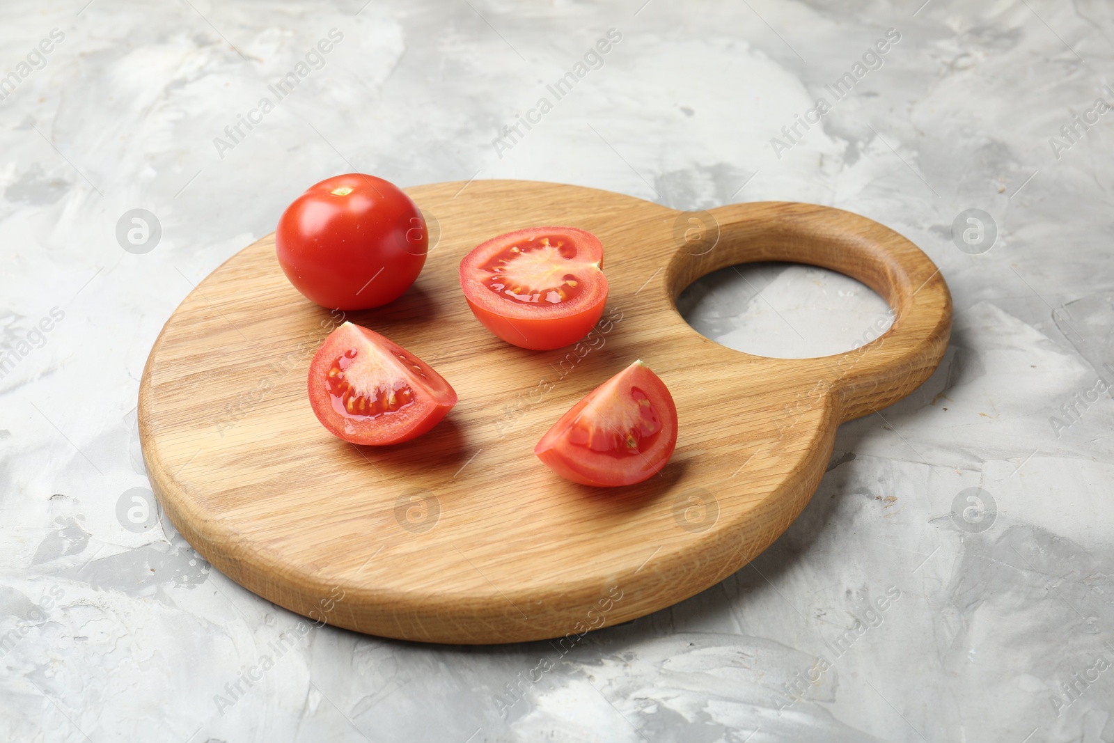 Photo of Cutting board with tomatoes on grey textured table, closeup