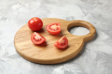 Photo of Cutting board with tomatoes on grey textured table, closeup