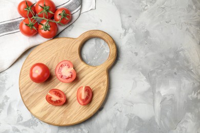 Photo of Cutting board with tomatoes on grey textured table, top view. Space for text