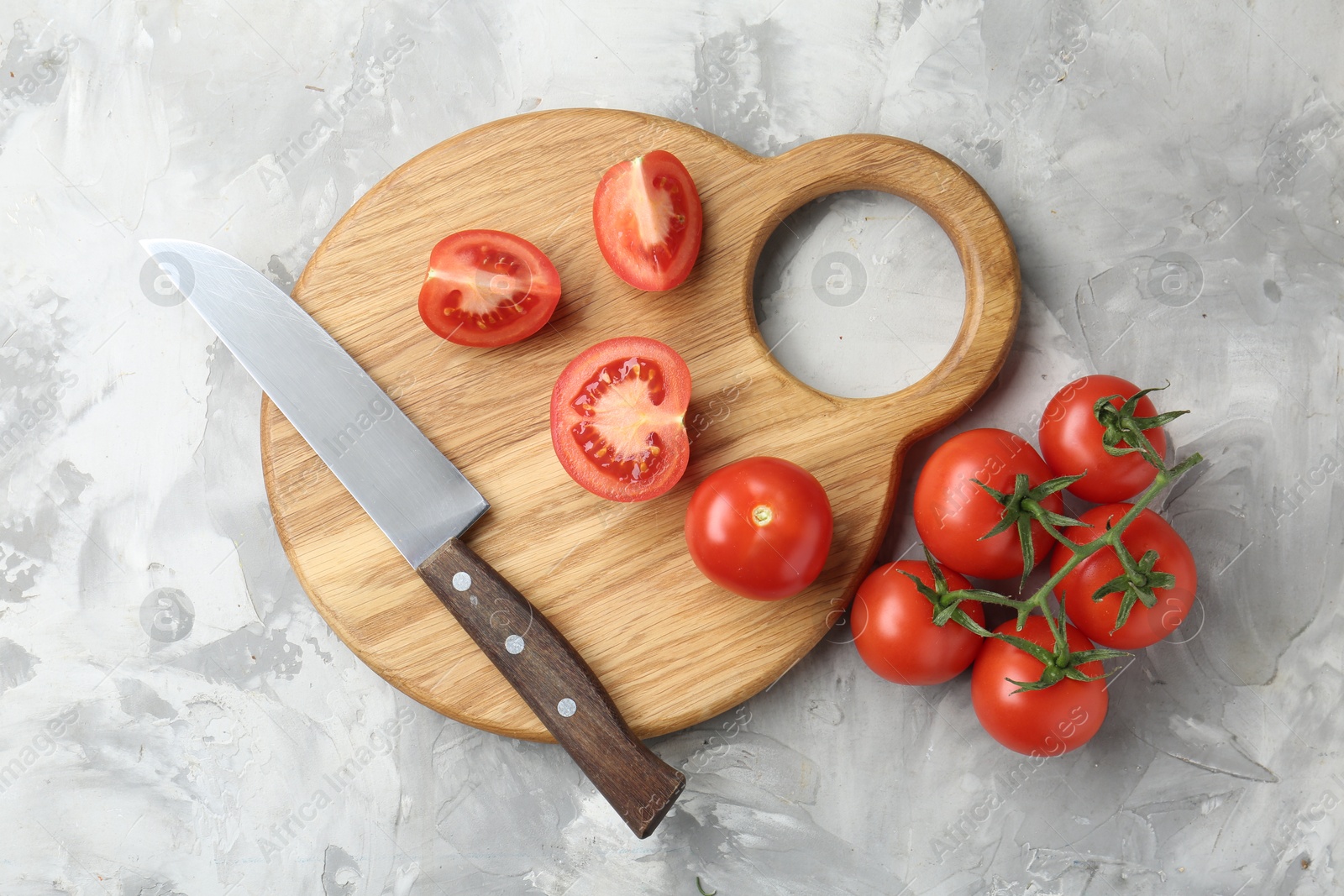 Photo of Cutting board with tomatoes and knife on grey textured table, top view